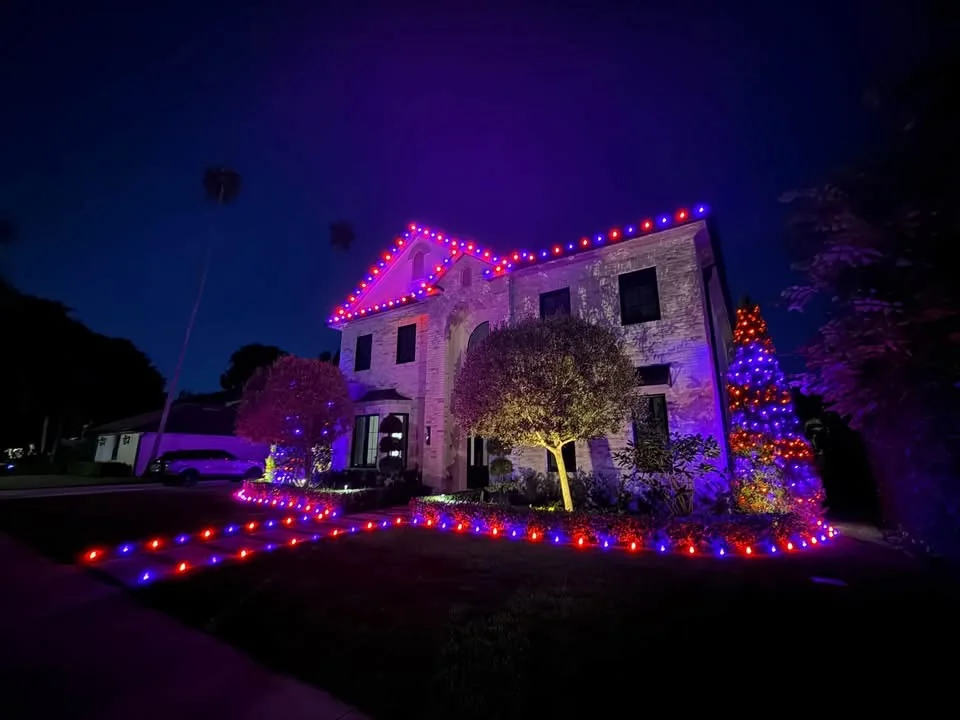Residential holiday display with orange and purple roofline, tree, and landscape lighting
