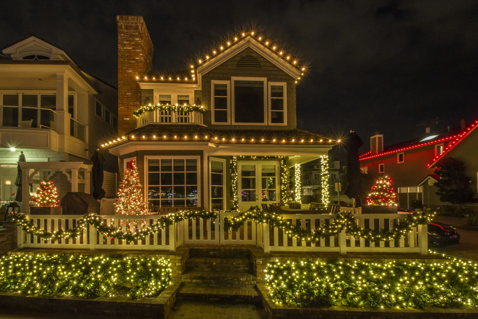 Illustrative residential exterior with warm-white roofline, porch, and landscape holiday lights at night