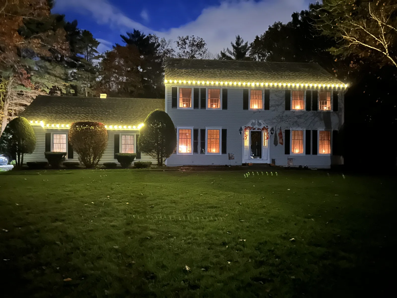 Warm-white holiday lights outlining a two-story home's roofline and attached wing at night
