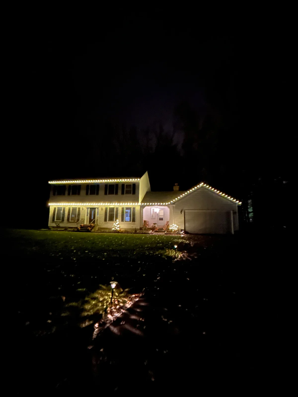 Warm-white holiday lights outlining a home's roofline, front entry, and garage gable at night