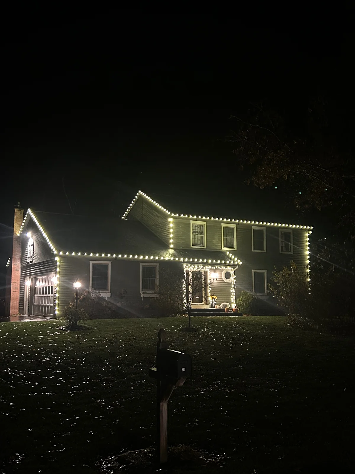 Warm-white holiday lights on a multi-level home's roofline and garage at night