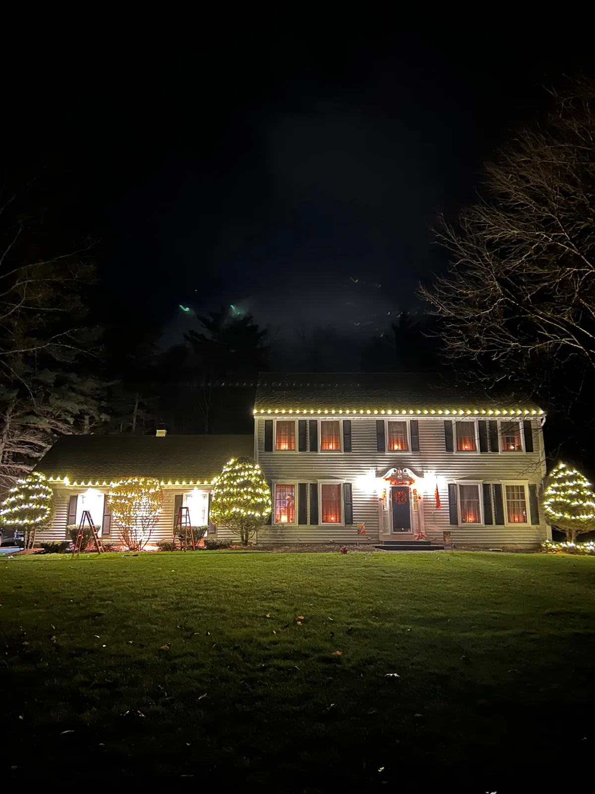 Classic home with warm-white holiday lights tracing the roofline, garage, and covered entry