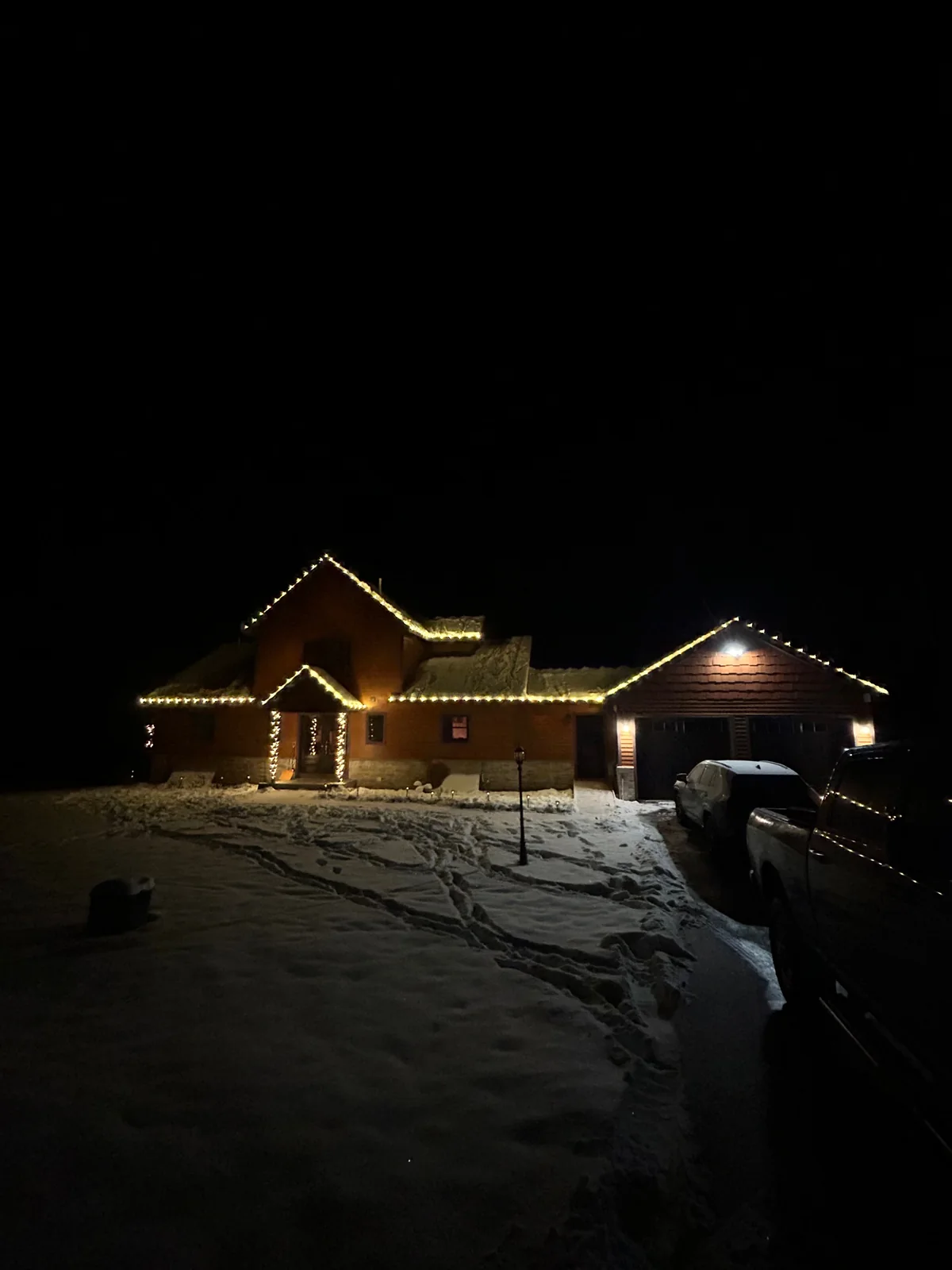 Stone-front home with warm-white holiday roofline, entry, and shrub lighting at night