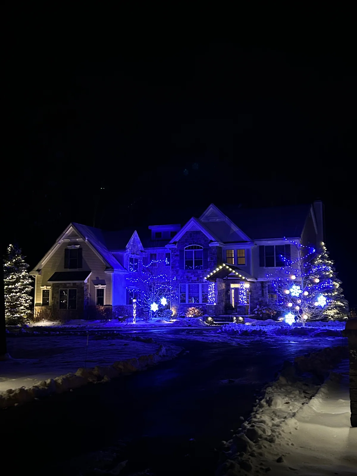 Warm-white holiday roofline lights framing a home on a snowy evening